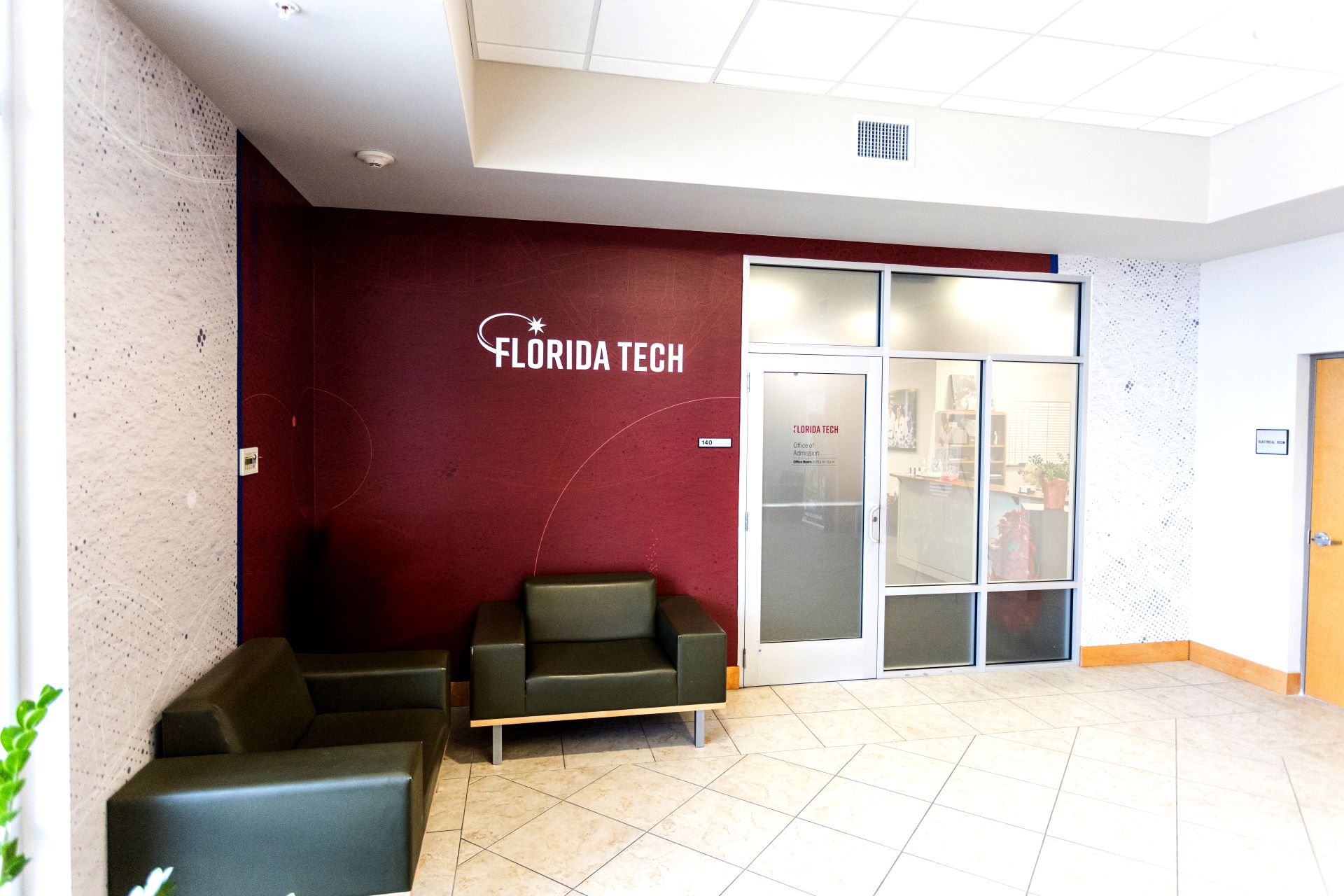 Interior view of the Florida Tech office, showcasing the entrance to the Office of Admission with modern seating arrangements, a maroon accent wall with the Florida Tech logo, and a well-lit reception area